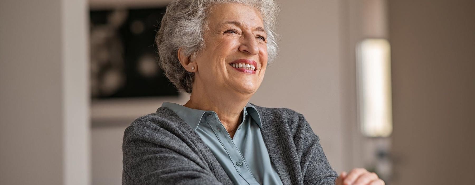 elderly woman with a cane, sits in a room and smiles